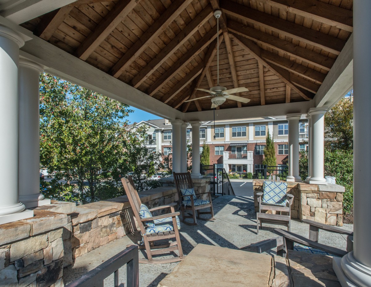 A cozy gazebo with rocking chairs under a wooden ceiling on a sunny day.