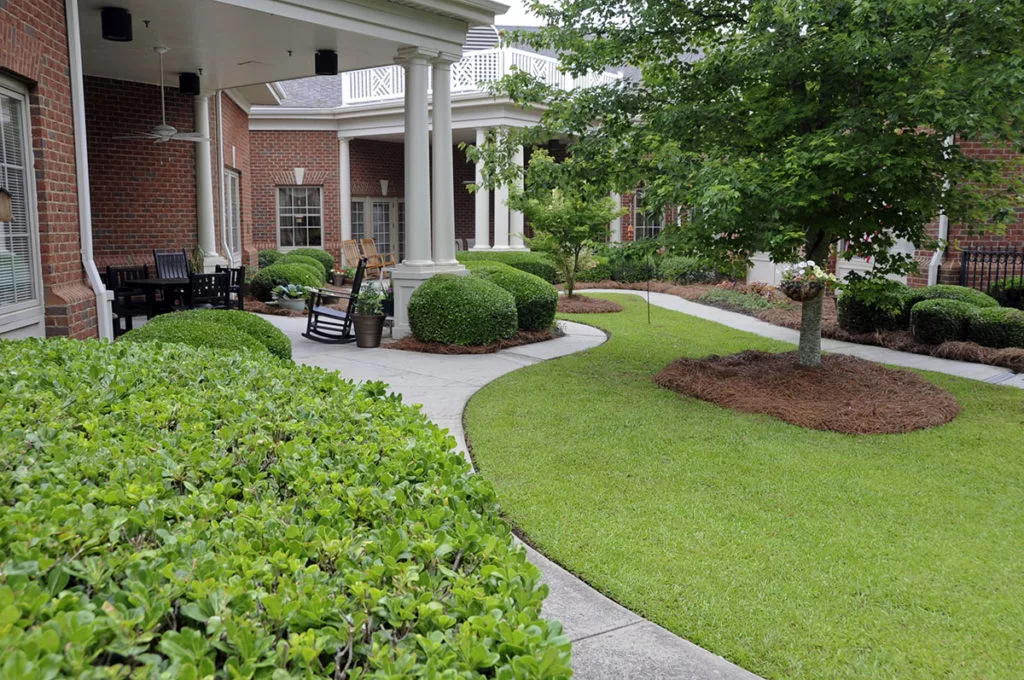 A beautifully landscaped outdoor area with a lush green lawn, carefully trimmed shrubbery, and a winding pathway.