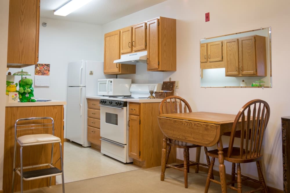 A cozy kitchen with wooden cabinets, equipped with a refrigerator, stove, and a dining table with chairs.