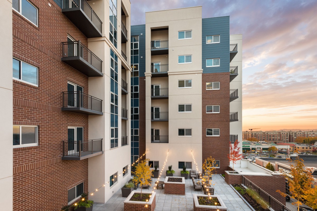 A modern apartment building with outdoor seating and a cityscape view at sunset.