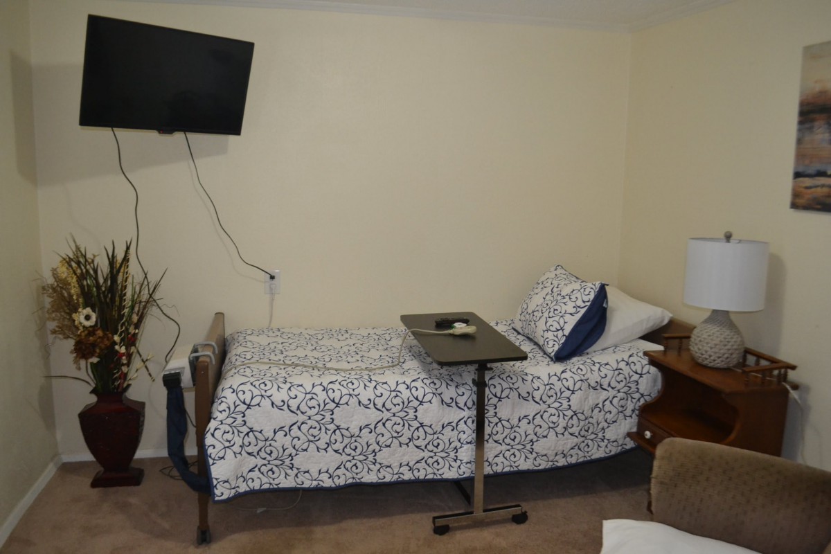 A hospital room with a single bed, wall-mounted television, and medical overbed table.