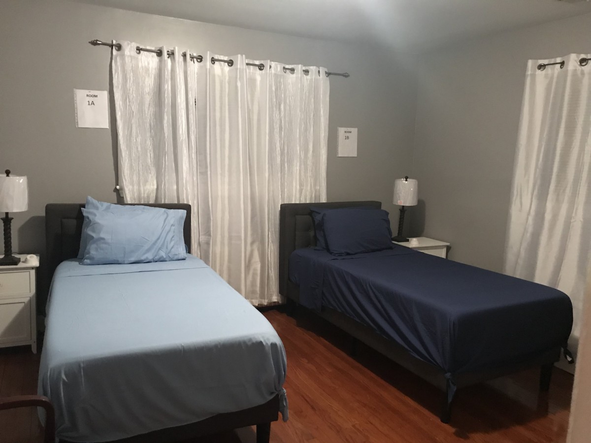 A small bedroom with two twin beds, a nightstand, and a lamp.