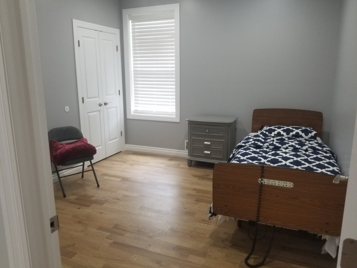 A simple bedroom with a bed, chair, and dresser on a wooden floor.