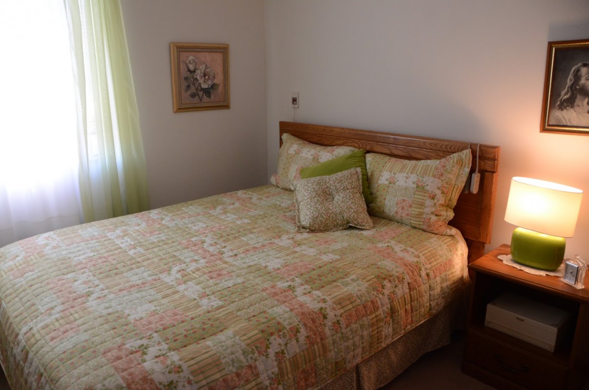 A cozy bedroom with a neatly made bed featuring a floral quilt and matching pillows.