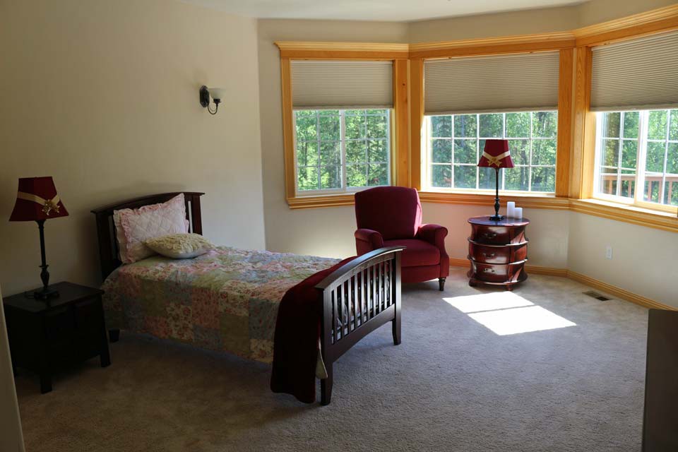 A cozy bedroom with a single bed and an armchair by the window, illuminated by natural light.