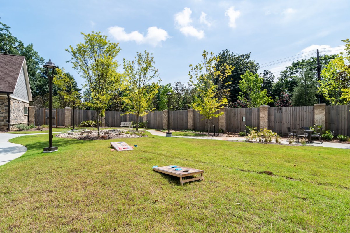 A grassy backyard with a cornhole game set up on a sunny day.