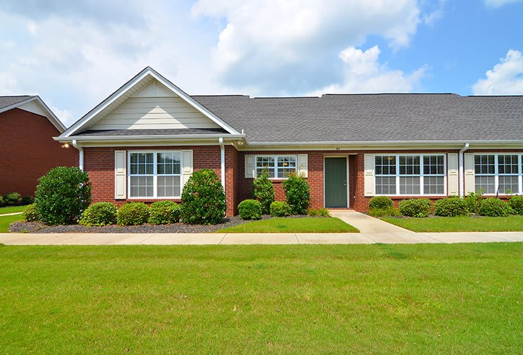 A suburban brick house with a well-maintained lawn and large windows.