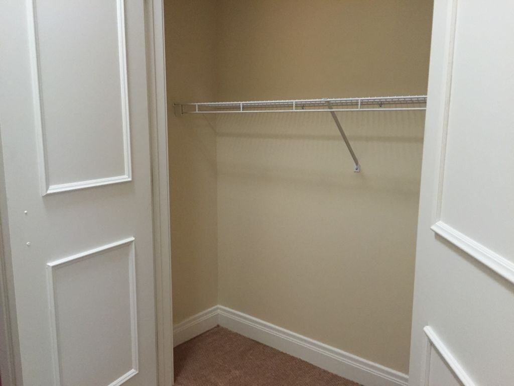 An empty indoor closet with a single shelf and hanging rod.
