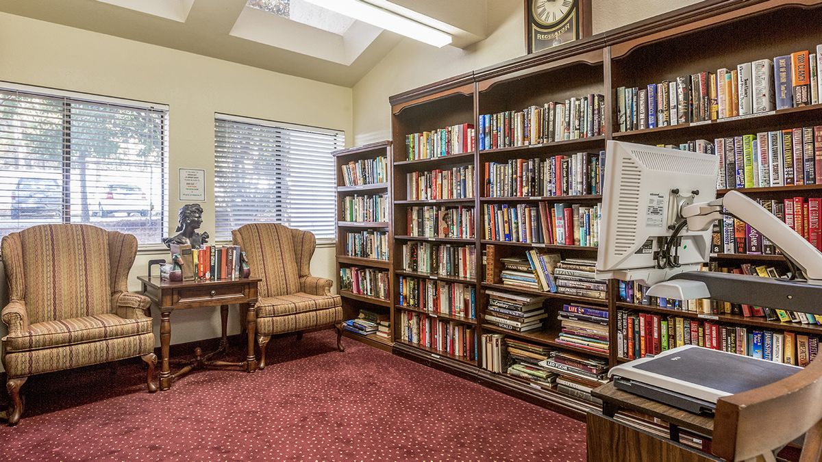 A cozy library room with bookshelves filled with books, an upholstered chair, and a carpeted floor.