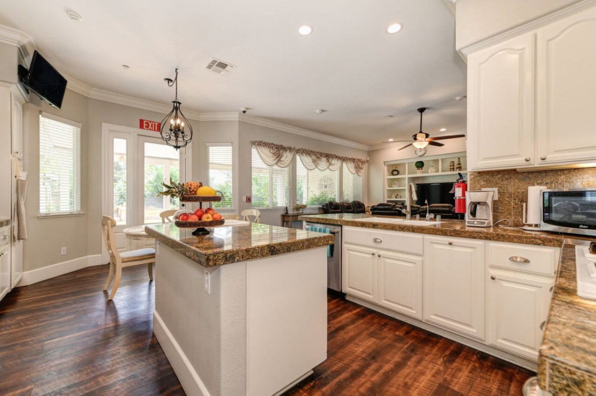 A modern kitchen with an island and white cabinetry, featuring wood flooring and ample natural light.