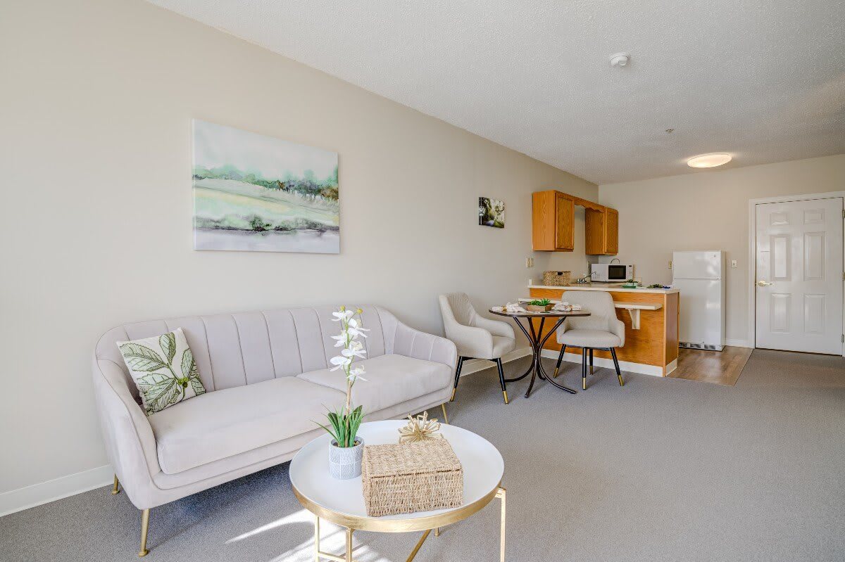 A cozy open-plan living area with a sofa, round table, and chairs leading into a compact kitchen.