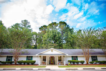 A suburban house with a front porch and surrounded by trees under a partly cloudy sky.