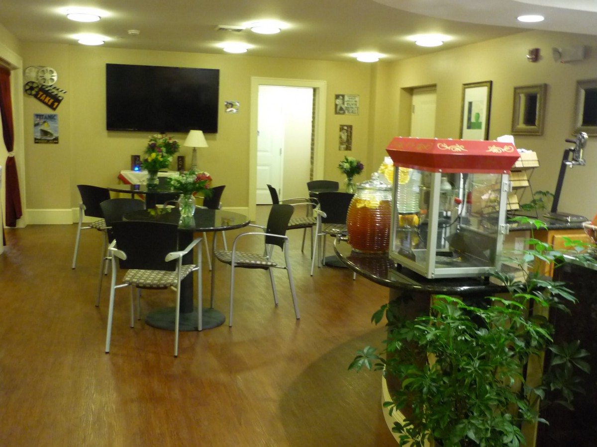 A cozy lobby area featuring tables and chairs, a popcorn machine, television, and decorative plants.