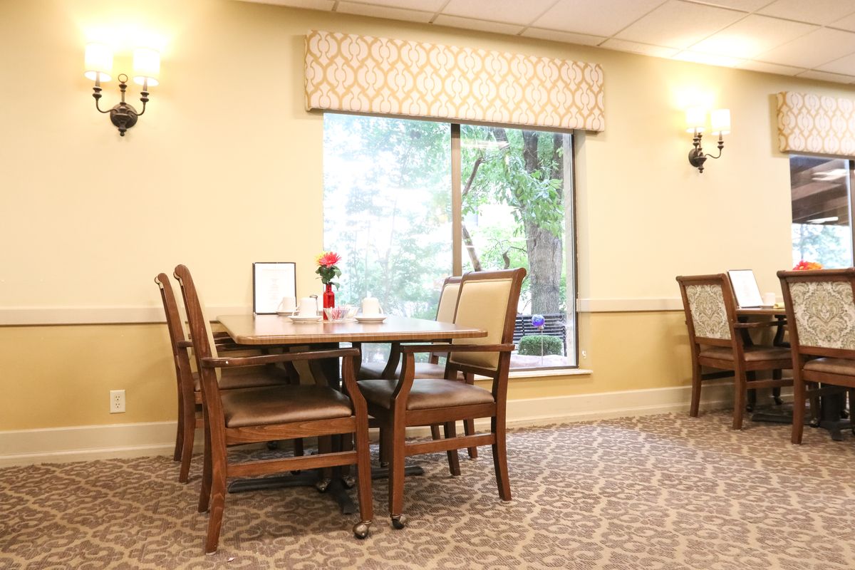 A cozy dining area with a table set near a large window, surrounded by cushioned chairs in a warmly lit room.