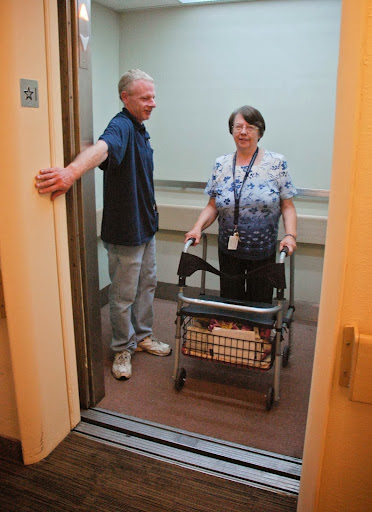 A person using a walker is assisted by another individual in an elevator.