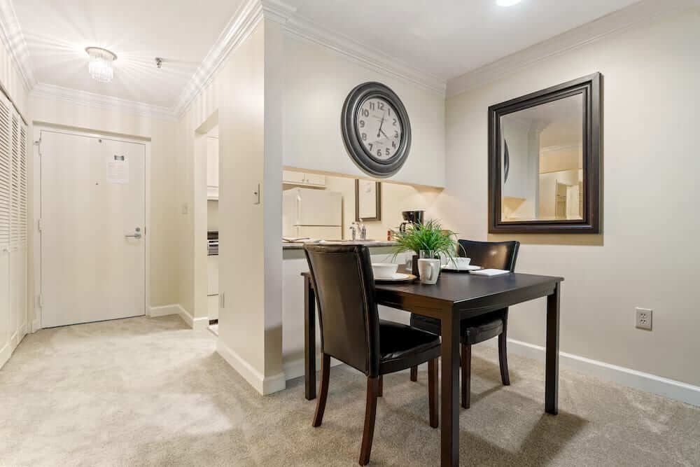 A modern dining area with a minimalist design, featuring a table and chairs, a decorative wall clock, and a large mirror.