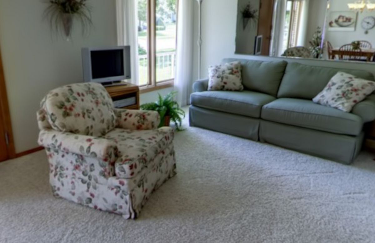 A cozy living room featuring a sofa, armchair, television, and large windows letting in natural light.