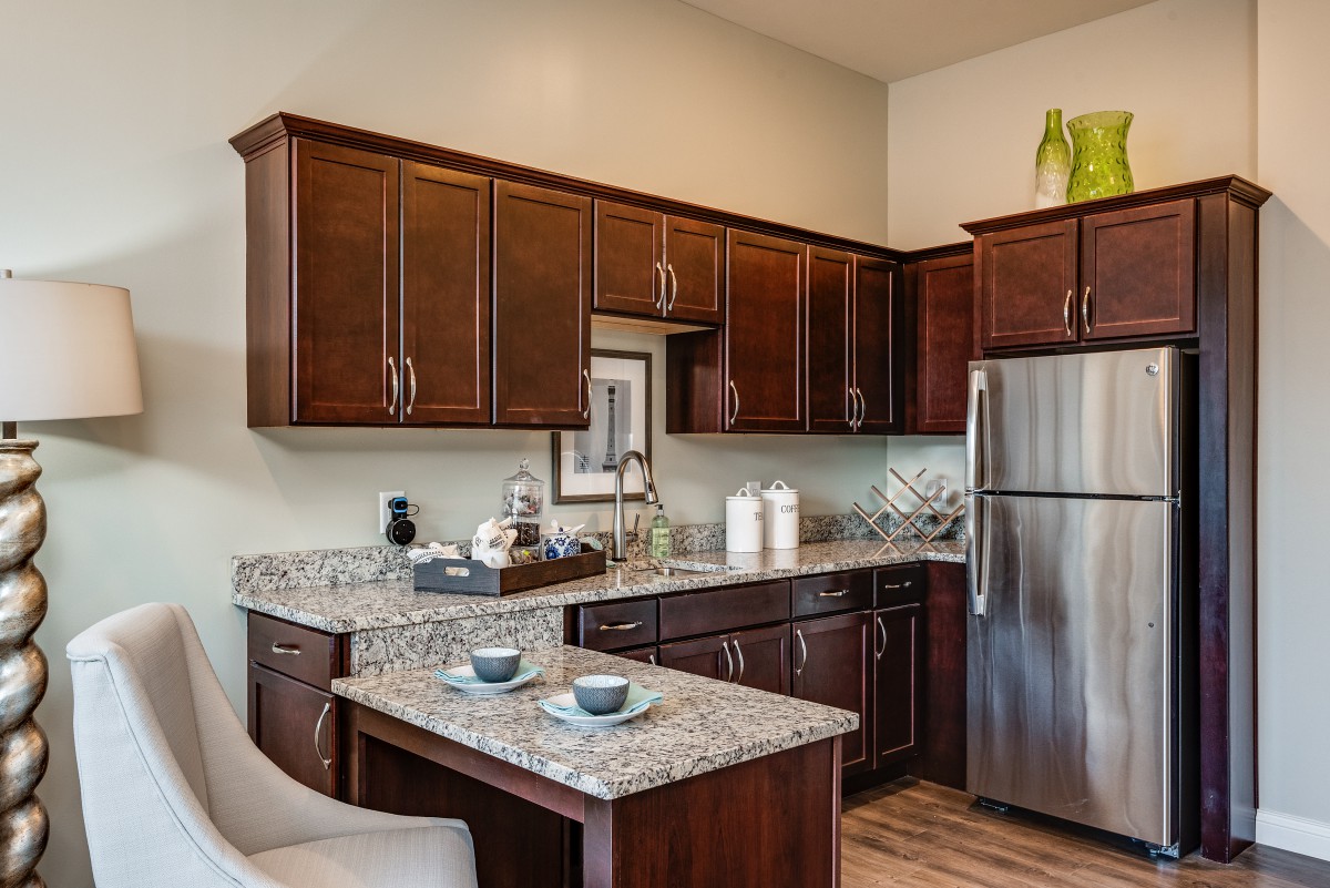 A modern kitchen with dark wood cabinets, granite countertops, and stainless steel appliances, featuring a small bar seating area.
