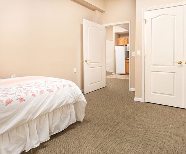 A simple bedroom with a bed, carpeted floor, and an open door leading to another room.