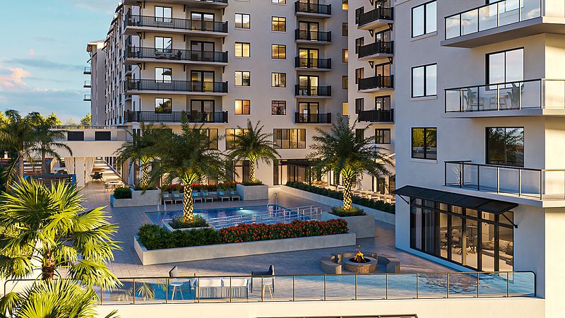 A modern residential apartment complex featuring a pool and palm trees in the outdoor courtyard during the evening.