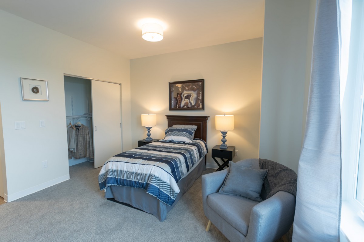A cozy bedroom with a single bed, two bedside lamps, and a comfortable chair.