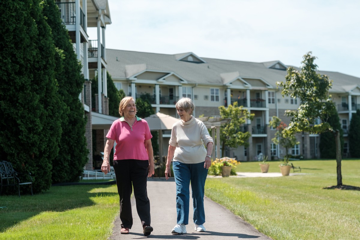 Two elderly people taking a walk outside a retirement community building.