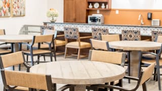 A cozy indoor dining area featuring wooden tables and chairs, with decorative elements and a coffee machine in the background.