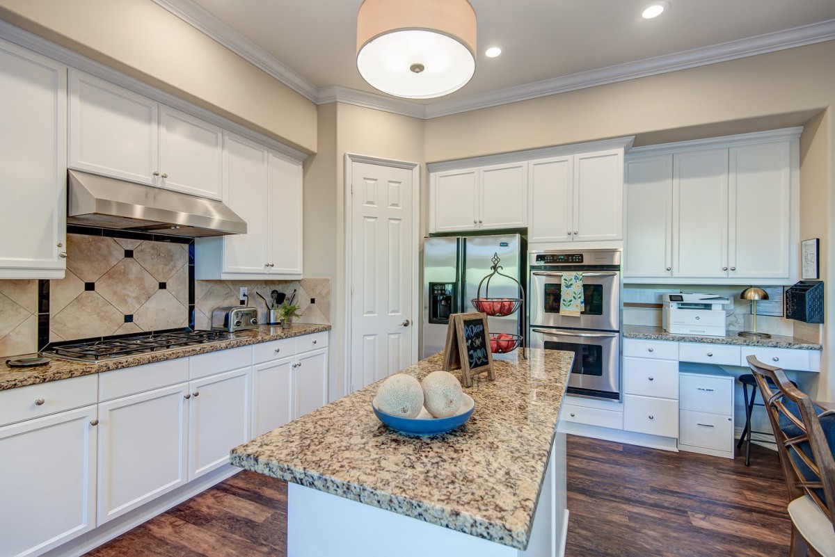 A modern kitchen featuring a central island with a granite countertop, white cabinetry, and stainless steel appliances.