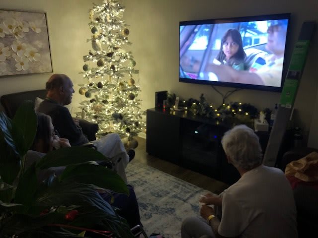 A family gathers around the TV in a decorated living room during Christmas.