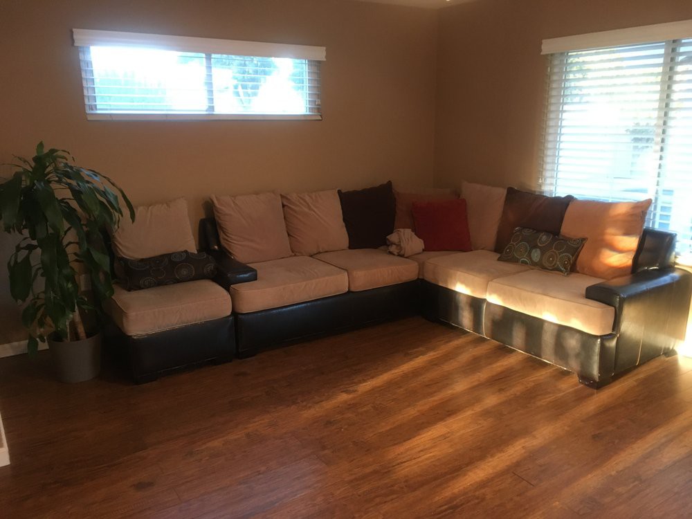 A cozy living room with a large sectional sofa and wooden flooring, bathed in natural daylight.