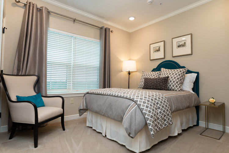 A well-decorated bedroom featuring a neatly made bed, a cozy chair, and soft lighting.