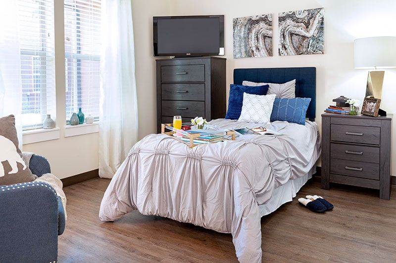 A cozy bedroom featuring a neatly made bed, a television on a dresser, and decorative artwork on the walls.