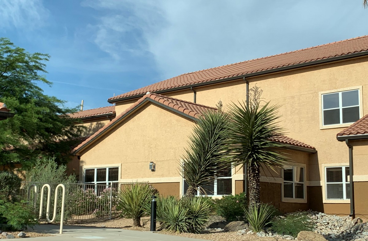 A house with a tiled roof, surrounded by desert landscaping under a partly cloudy sky.