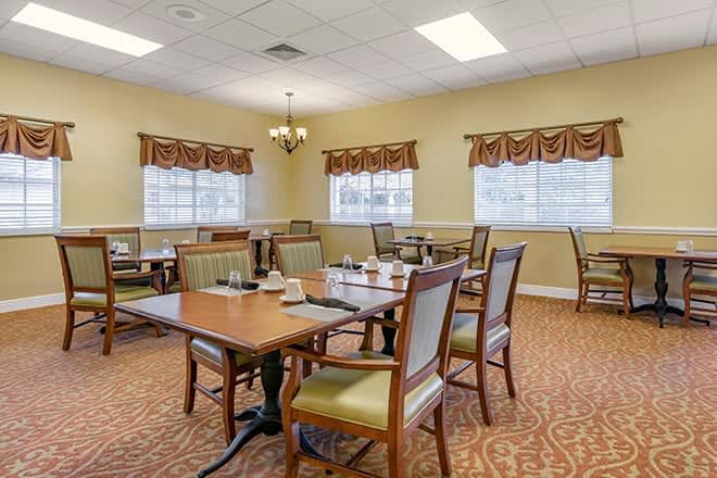 A dining area with neatly arranged tables and chairs, featuring windows with curtains.