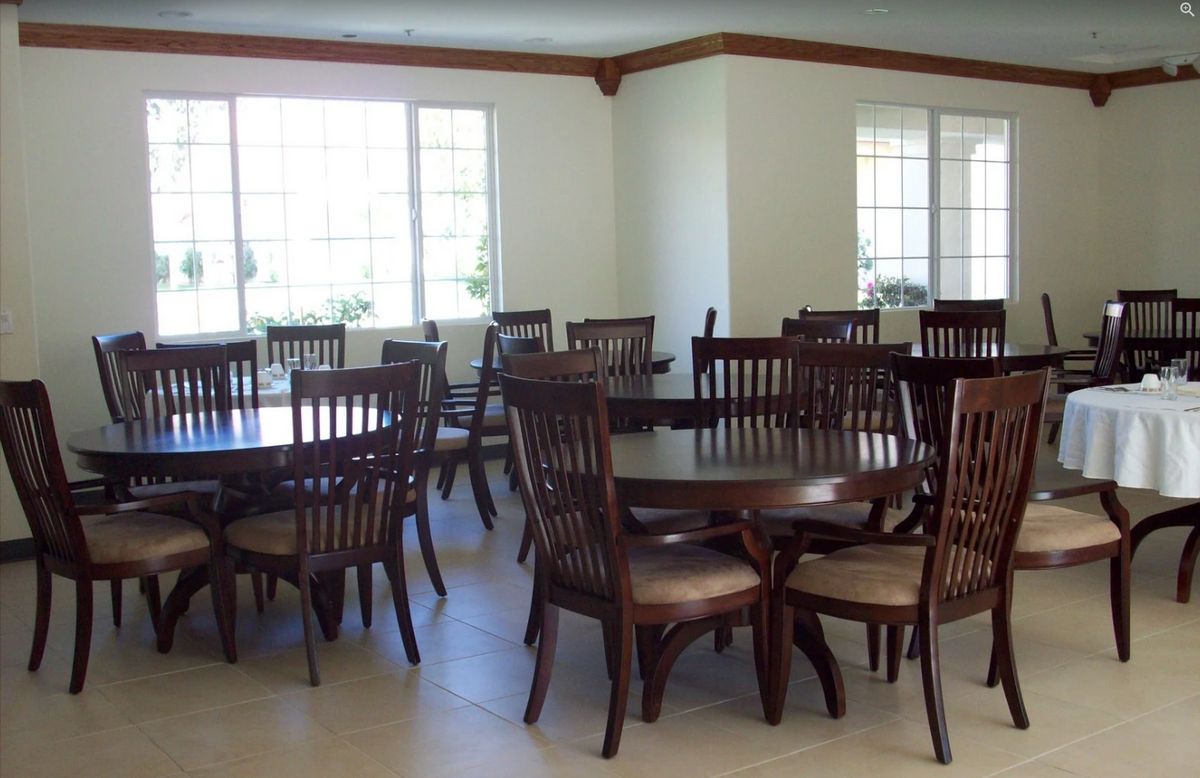 An empty dining area with multiple wooden tables and chairs arranged near large windows.