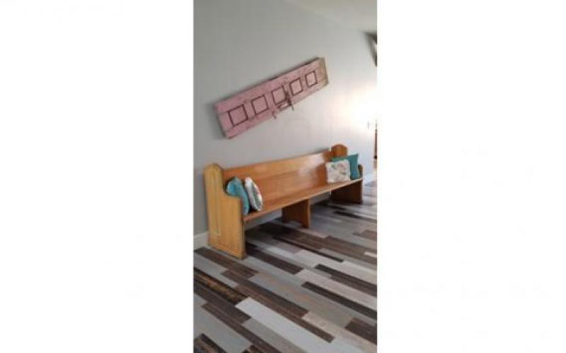 A wooden bench with cushions next to a wall, adorned with artwork above and set on a patterned carpet floor.