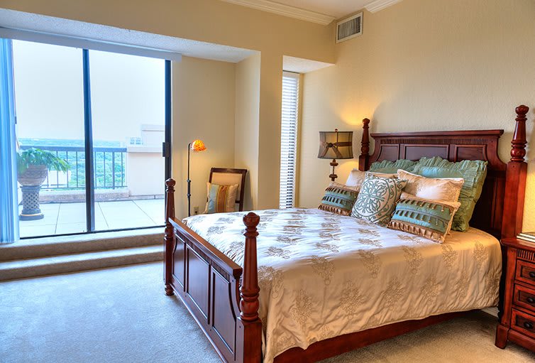 A cozy bedroom with a wooden bed, decorative pillows, and a view of the balcony.