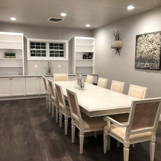 A modern dining room featuring a large table with eight chairs, elegant lighting, and artwork on the wall.