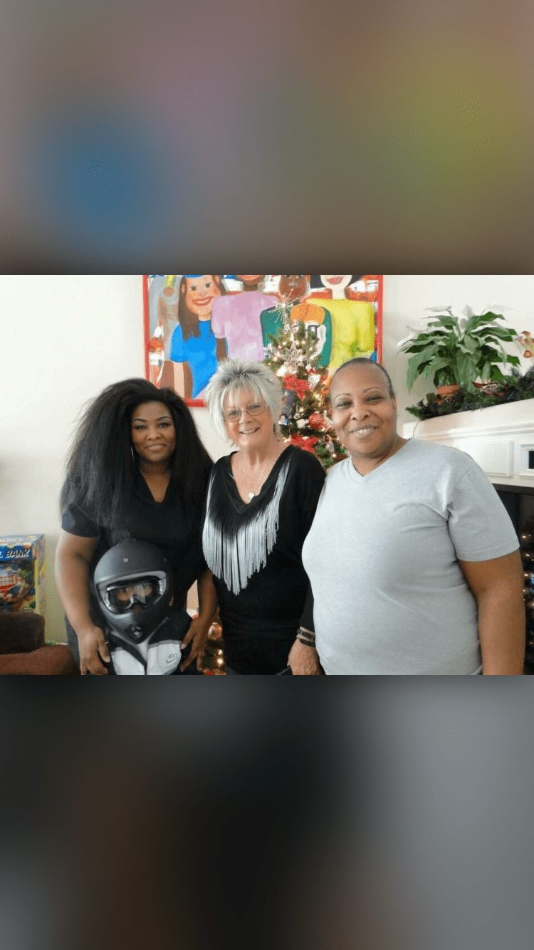 Three people smiling indoors with plants in the background.