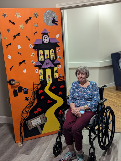 An elderly person sitting in a wheelchair next to a vibrant Halloween-themed backdrop.