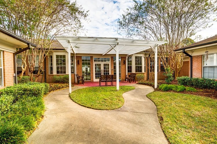 A charming house with a pathway leading to a covered patio surrounded by greenery.