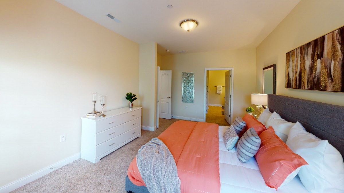 A cozy and modern bedroom with an orange-themed decor, featuring a bed, dresser, and soft lighting.