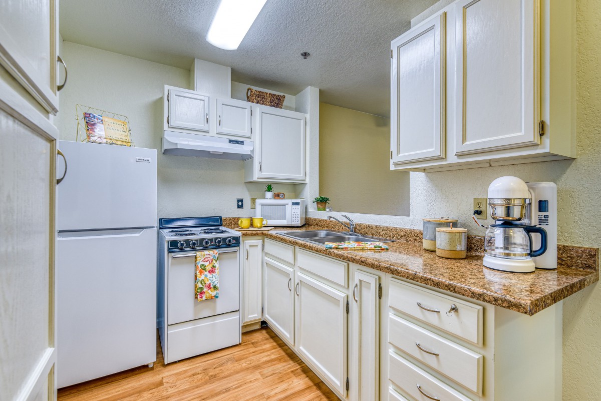 A cozy kitchen with white cabinets, a refrigerator, stove, and various countertop appliances.