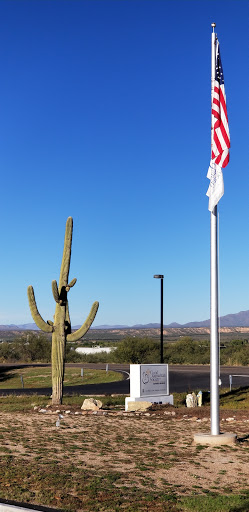 A saguaro cactus stands tall alongside a flag against a clear blue sky in a desert landscape.