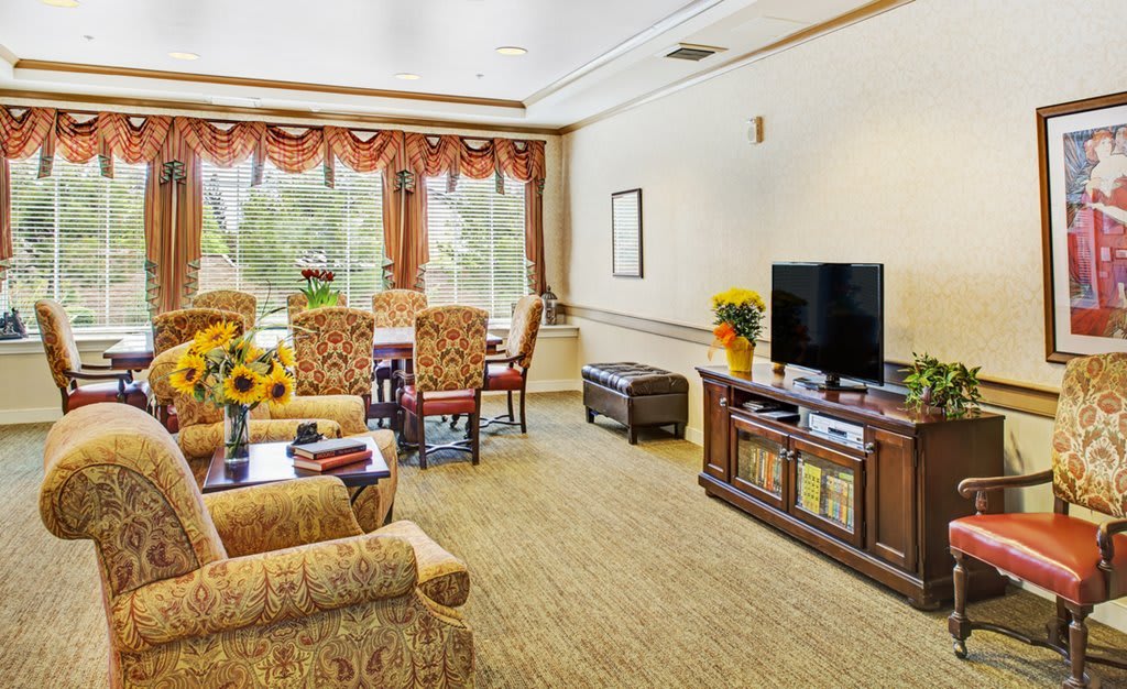 A cozy living room with a dining area, featuring comfortable seating, a television, and large windows.