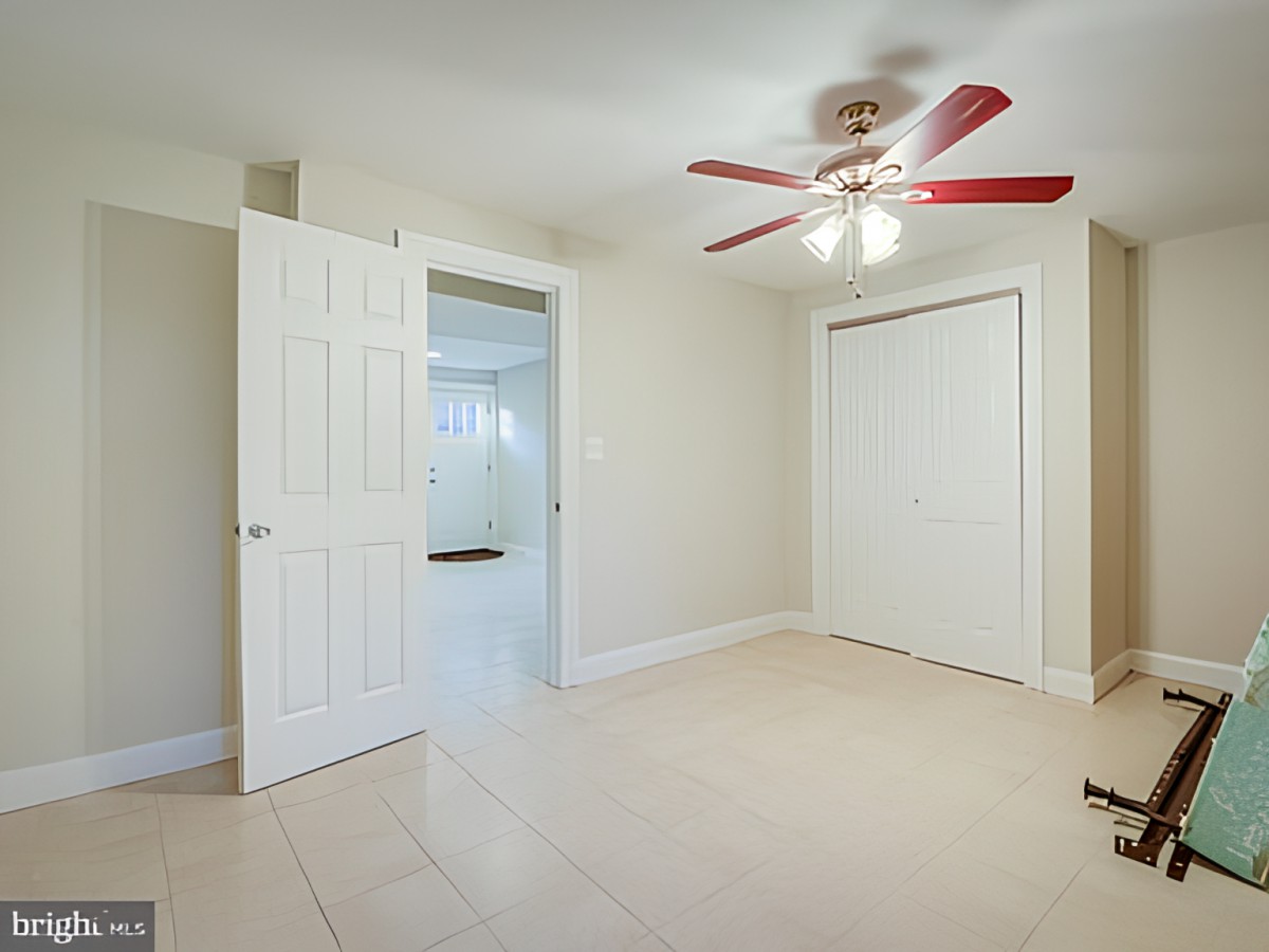 An empty bedroom with a ceiling fan, tile flooring, a closed closet, and an open doorway.