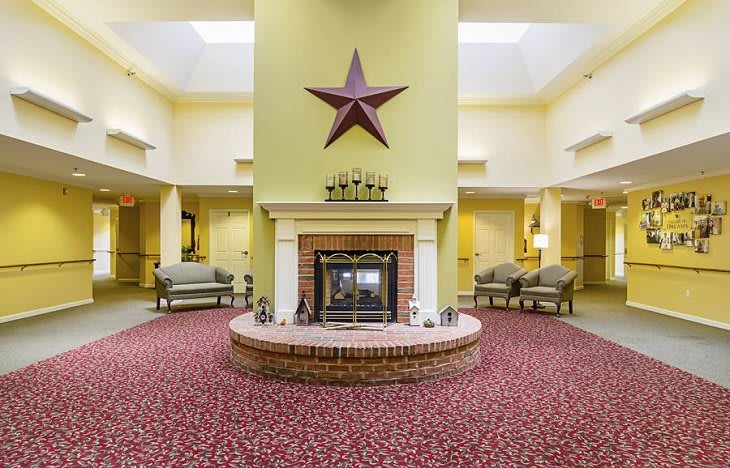 A welcoming lobby interior featuring a central fireplace with a large star decoration above, surrounded by comfortable seating and patterned carpet.