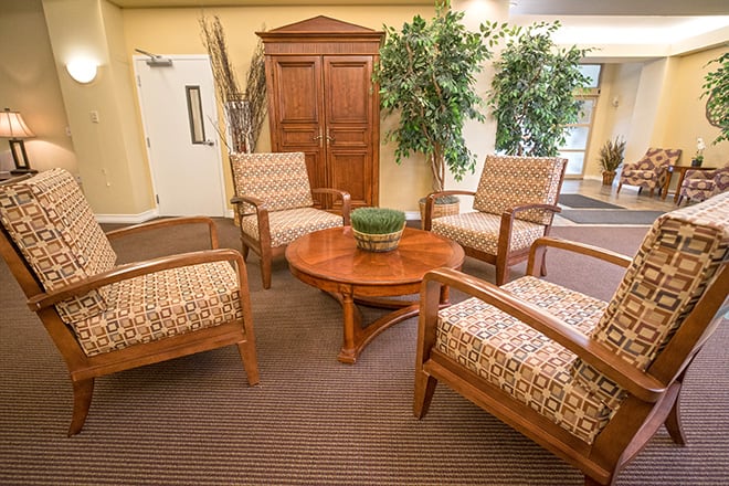 A cozy lobby area with four patterned chairs around a wooden coffee table, accented by greenery.