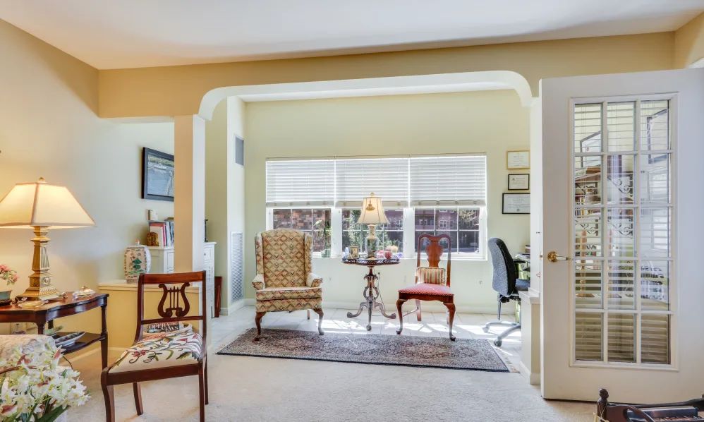 A cozy living area featuring classic armchairs, a desk setup by the window, and elegant decor elements.