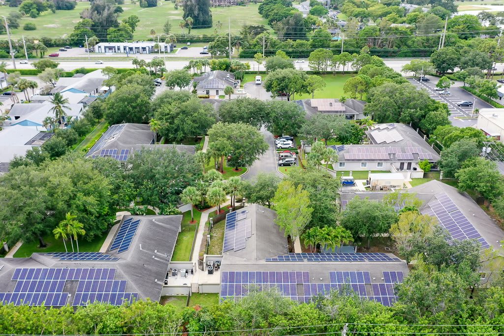 Aerial view of a neighborhood with houses equipped with solar panels surrounded by ample greenery.